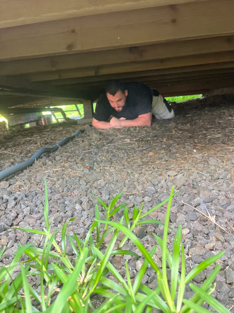 Une personne allongée sous une terrasse en bois, sur un chantier.
