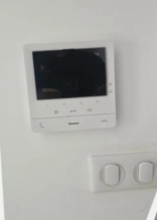 L'écran d'un visiophone Bticino posé au mur, au-dessus de deux interrupteurs.