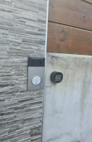 La platine du visiophone et un clavier à code, posés à l'entrée sur un mur en pierre et en béton.